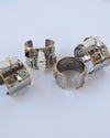 Four hammered metal cuff bracelets with gold trim and turquoise, white, and green stone accents, arranged on a light gray background.