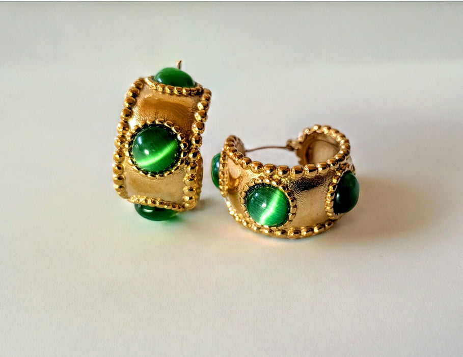 Gold earrings with green gemstones on a light gray background