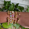Gold bracelets with gemstones on a wrist against a plant background