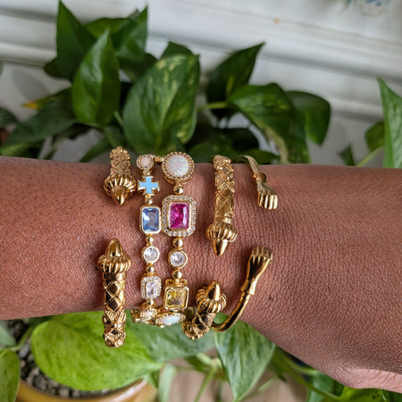 Gold bracelets with gemstones on a wrist against a plant background