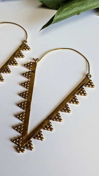 Gold triangle-shaped earrings on a white surface with green leaves.