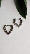 Pair of silver hoop earrings on a white surface with a green leaf.