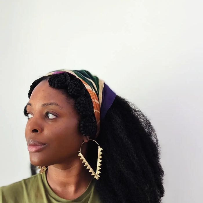 Woman wearing a colorful headscarf and gold earrings against a white background