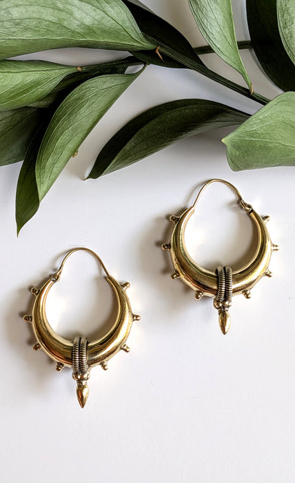 Gold hoop earrings on a white surface with green leaves in the background