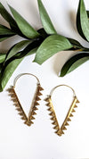 Gold hoop earrings with decorative elements on a white background with green leaves.