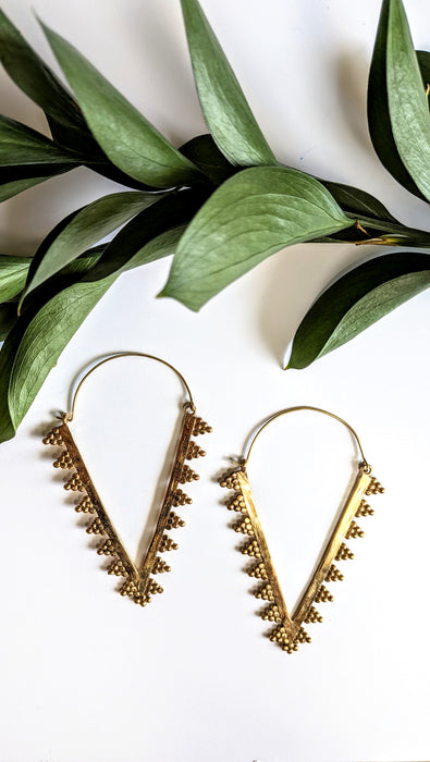 Gold hoop earrings with decorative elements on a white background with green leaves.