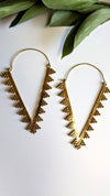 Gold earrings with leaf-like designs on a white background with green leaves.